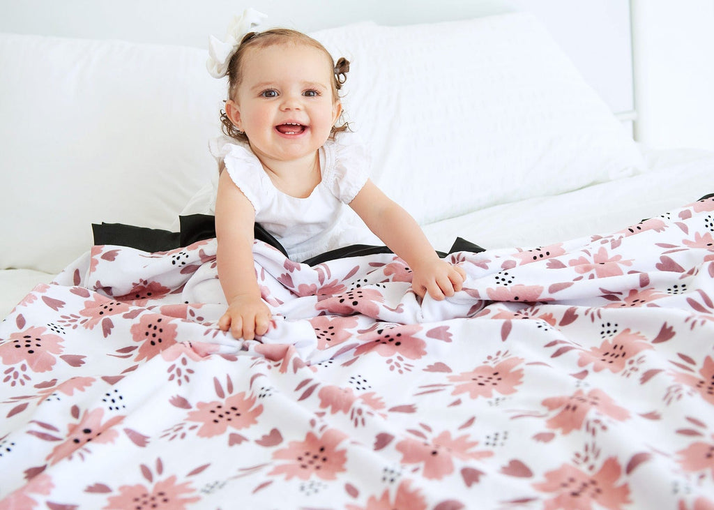 Toddler girl sitting under a pink apricot blossom themed blanket. 