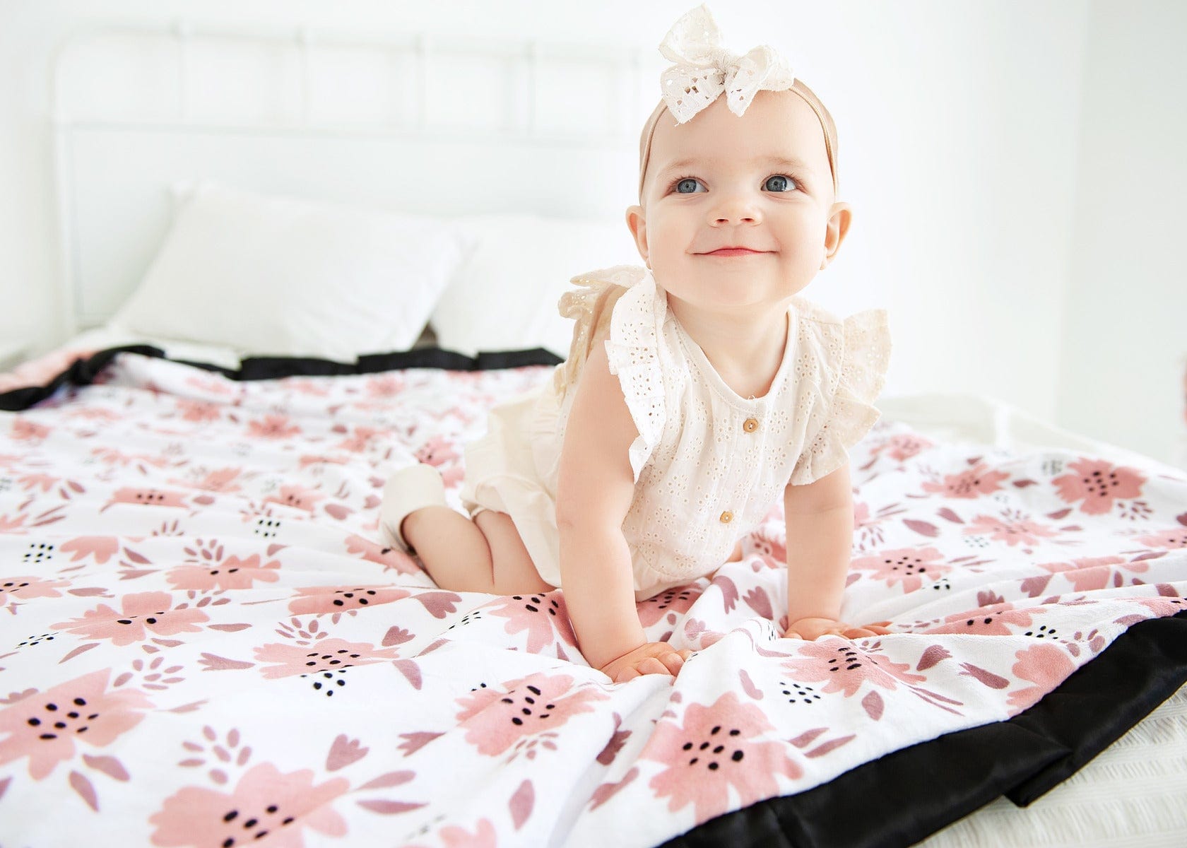 Baby girl sitting on a blush pink apricot blossom blanket .