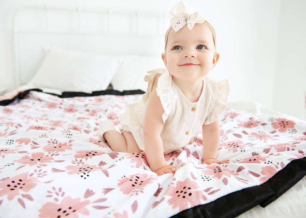 Baby girl sitting on a blush pink apricot blossom blanket .