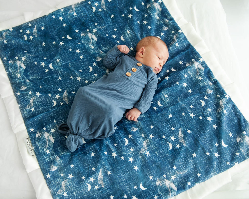 Infant boy laying on a navy blue blanket with cream stars and moons on it. 