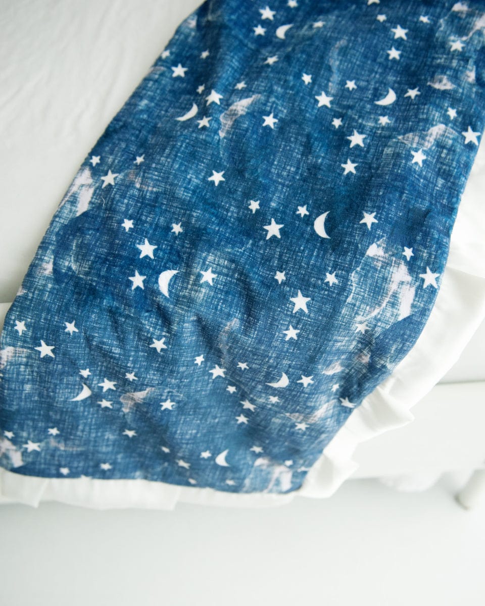 Navy blue blanket with cream stars and moons on it laid over the bottom corner of a bed.