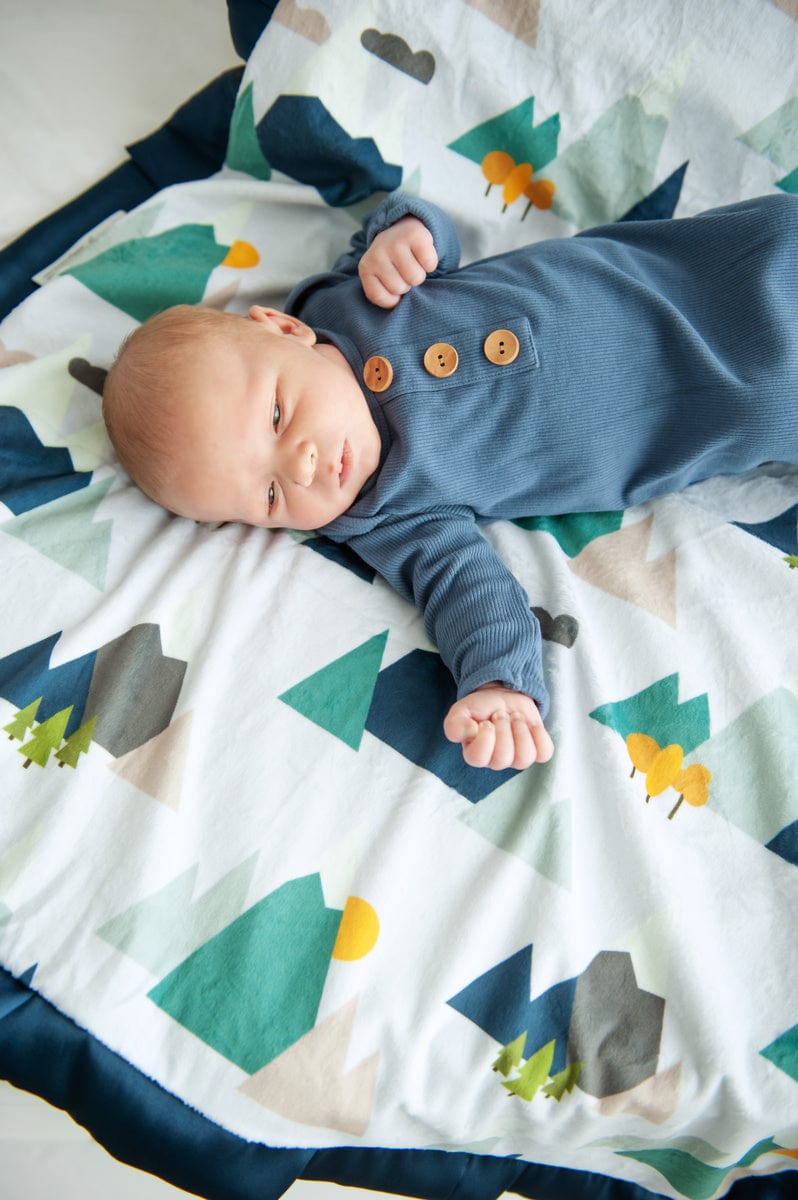 Baby boy laying on a blanket with a simple mountaintop pattern on it. 