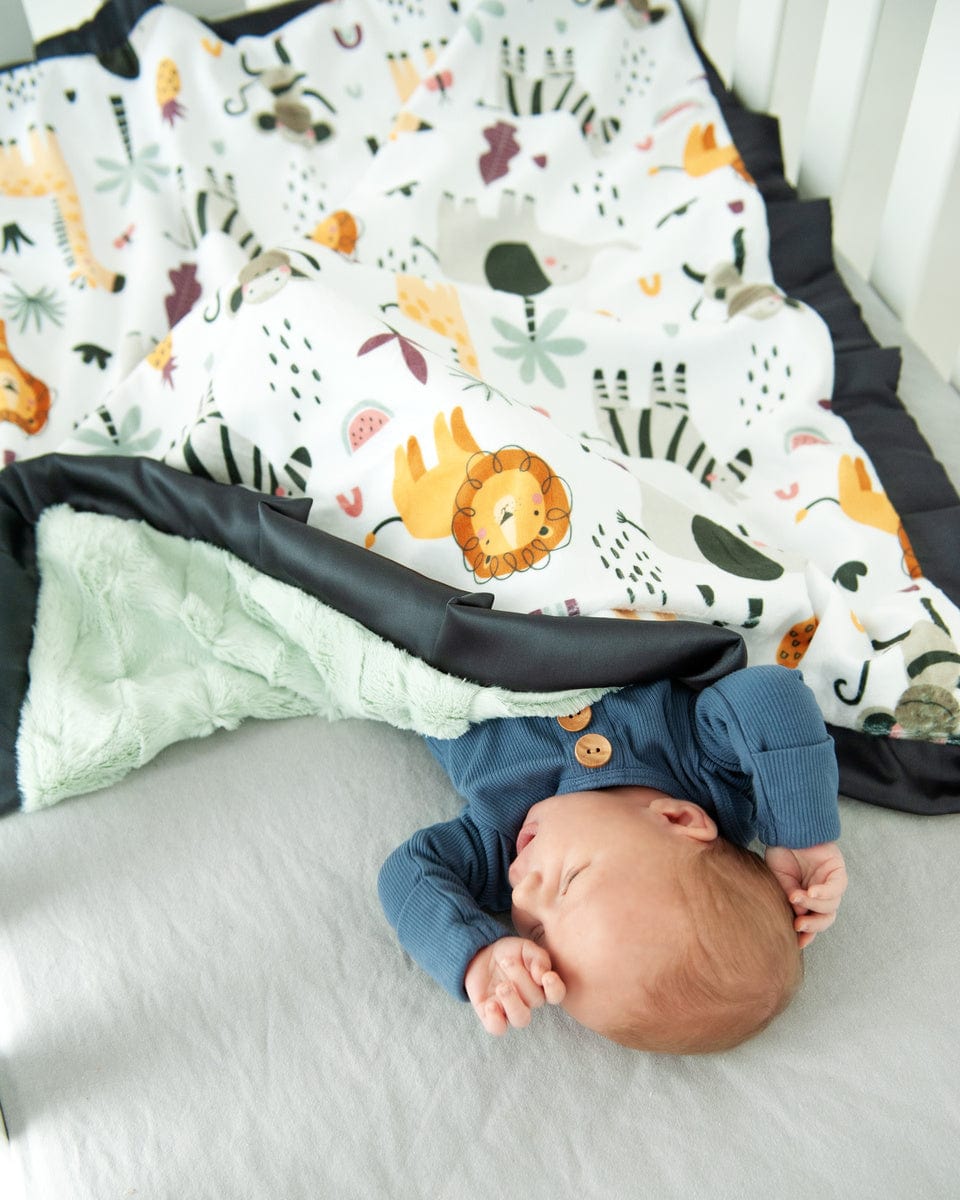 Baby boy laying in a crib with a cartoon zoo animal themed blanket.