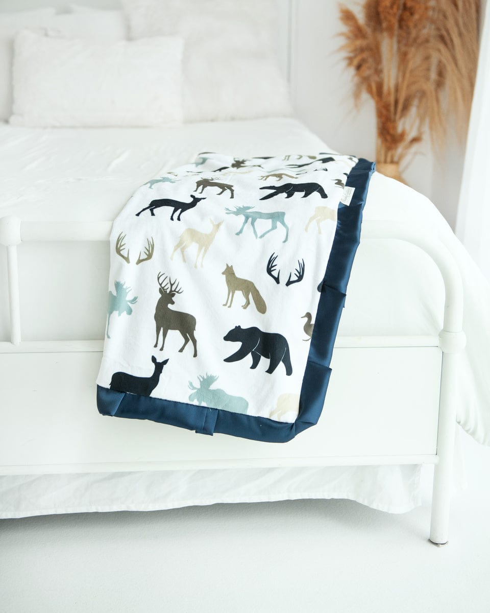 Teton woodland animal blanket by minky couture folded and hanging over the end of a bed.