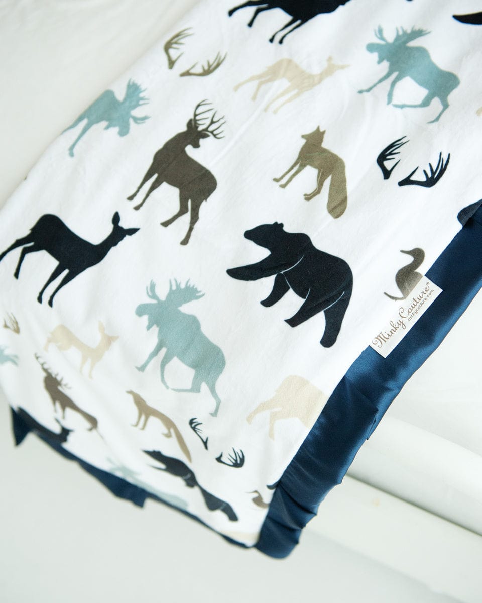 Teton woodland animal blanket by minky couture folded and hanging over the end of a bed.