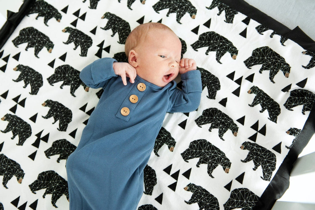 Newborn baby laying on top of a bear patterned blanket. 