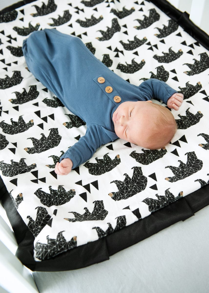 Newborn baby boy laying on top of a bear and triangle patterned blanket. 