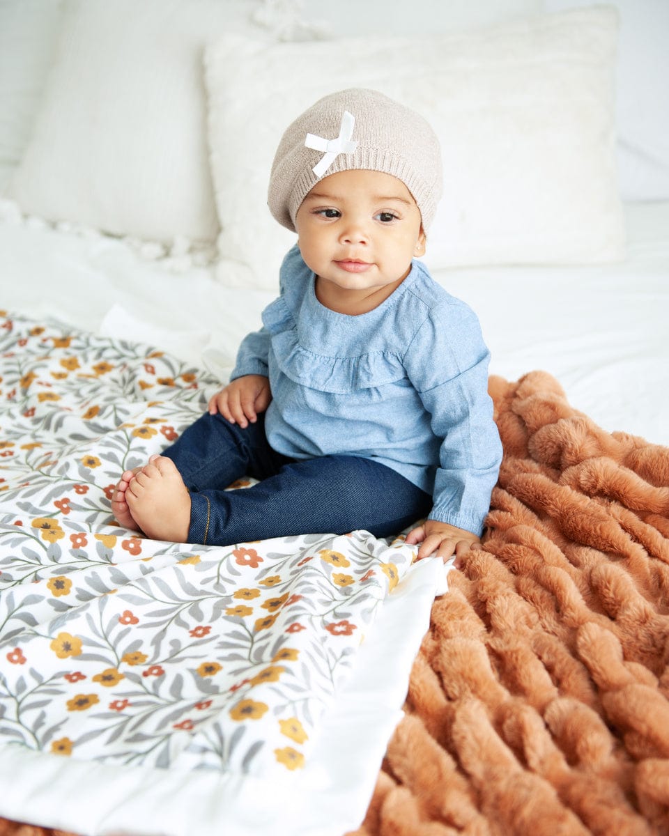 Baby girl sitting on a floral blanket with small copper and mustard flowers and gray greenery on it. 