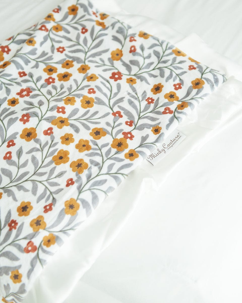 Floral blanket with small copper and mustard flowers and gray greenery laid over the end of a bed. 