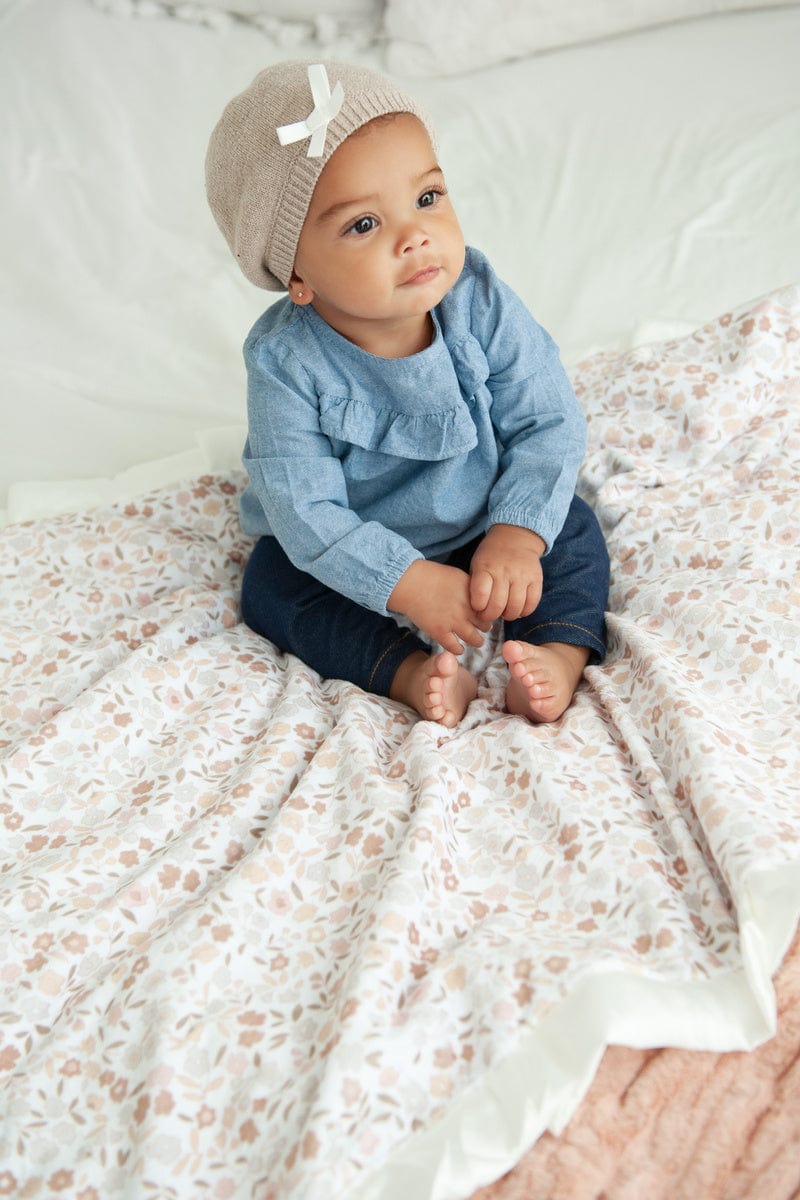 Baby girl sitting on top of a floral blanket with small flowers and greenery on it in shades of blush.