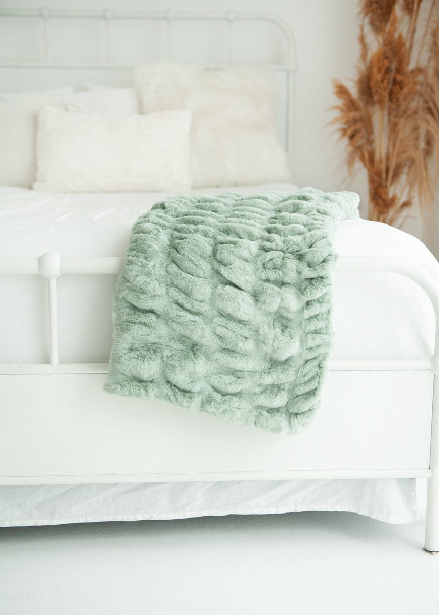 Light green ruched blanket folded and hanging from the end of a bed