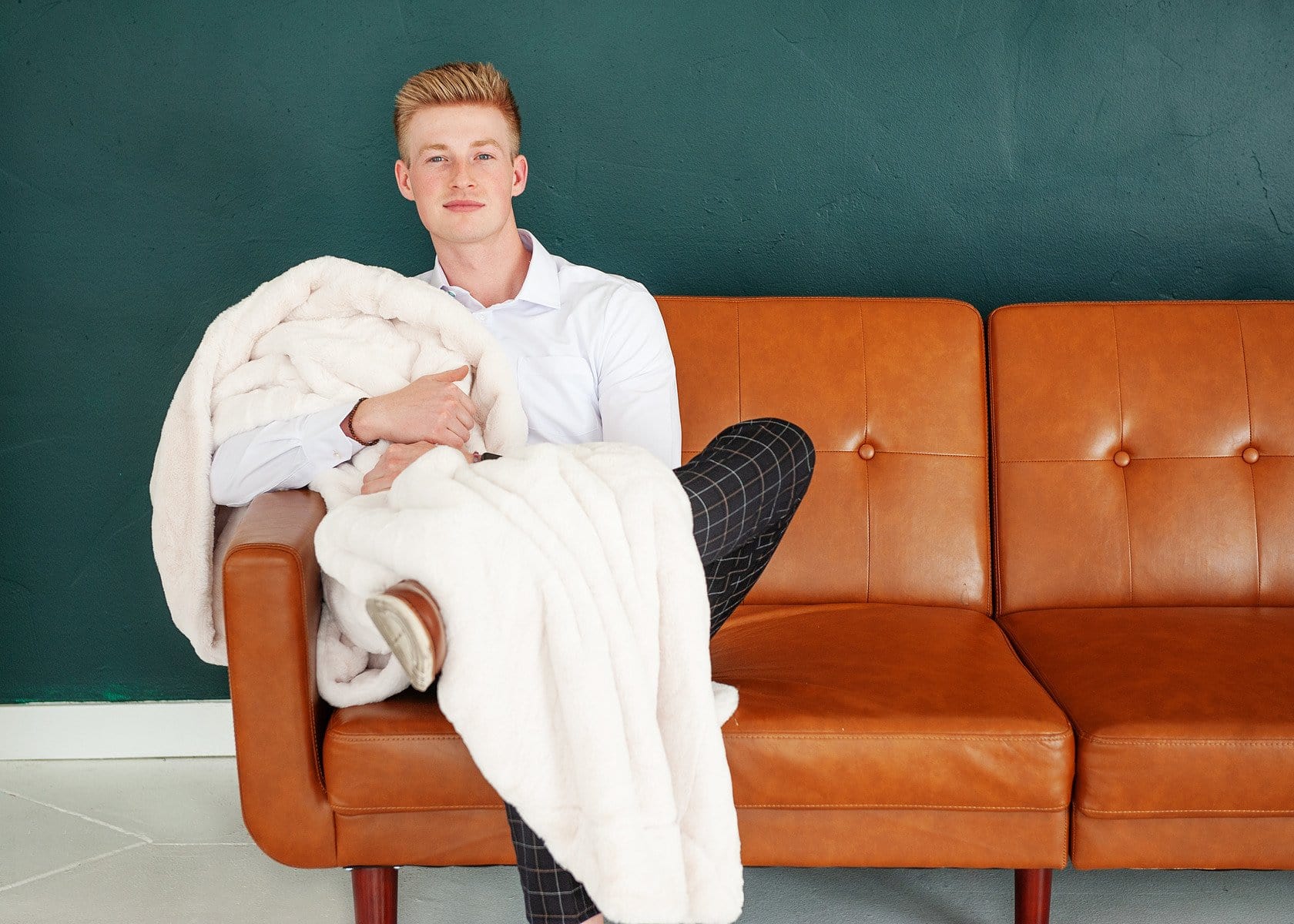 Young man sitting on a couch holding a thick cream plush blanket.