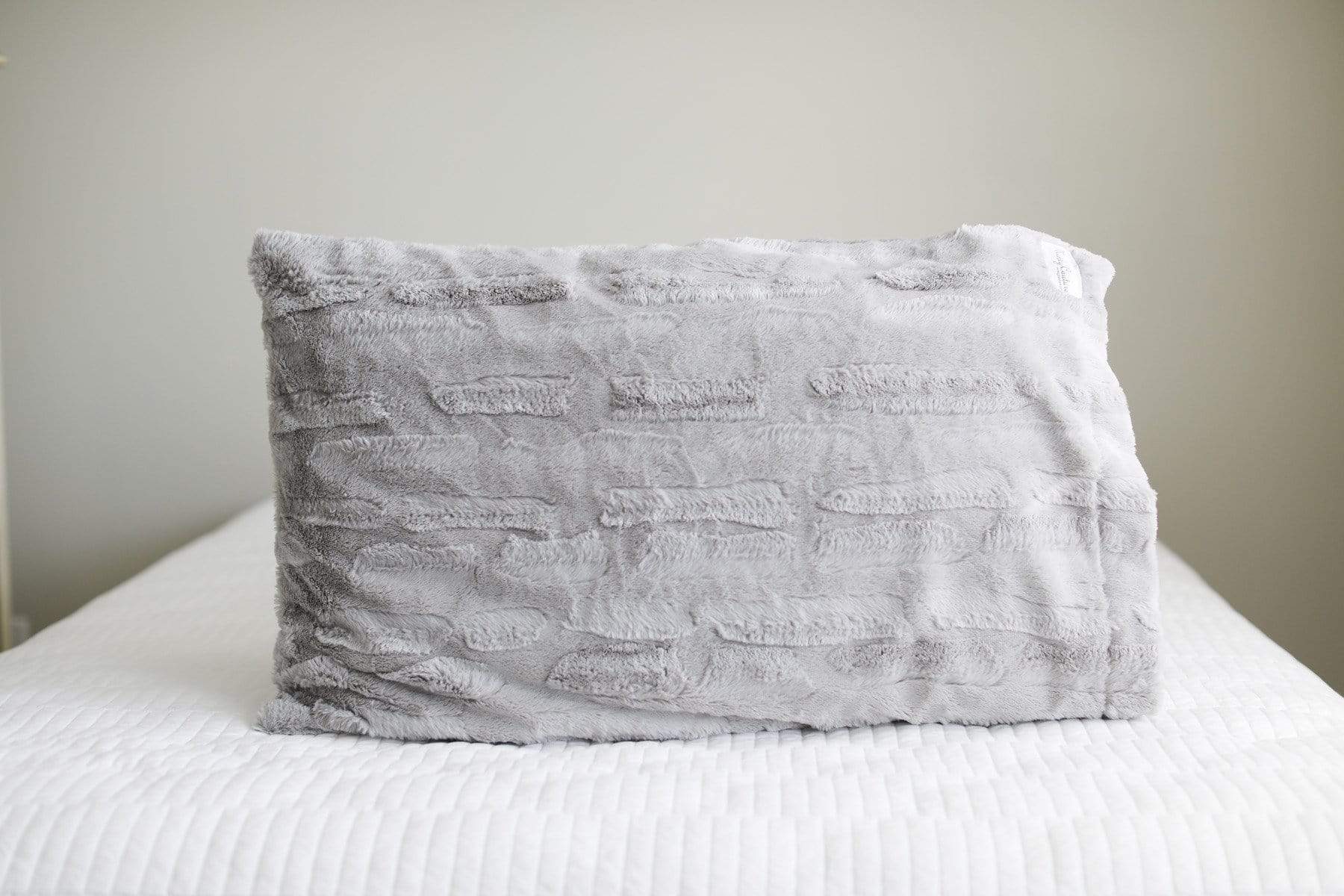 Light gray plush Minky Couture pillowcase sitting on a bed. 