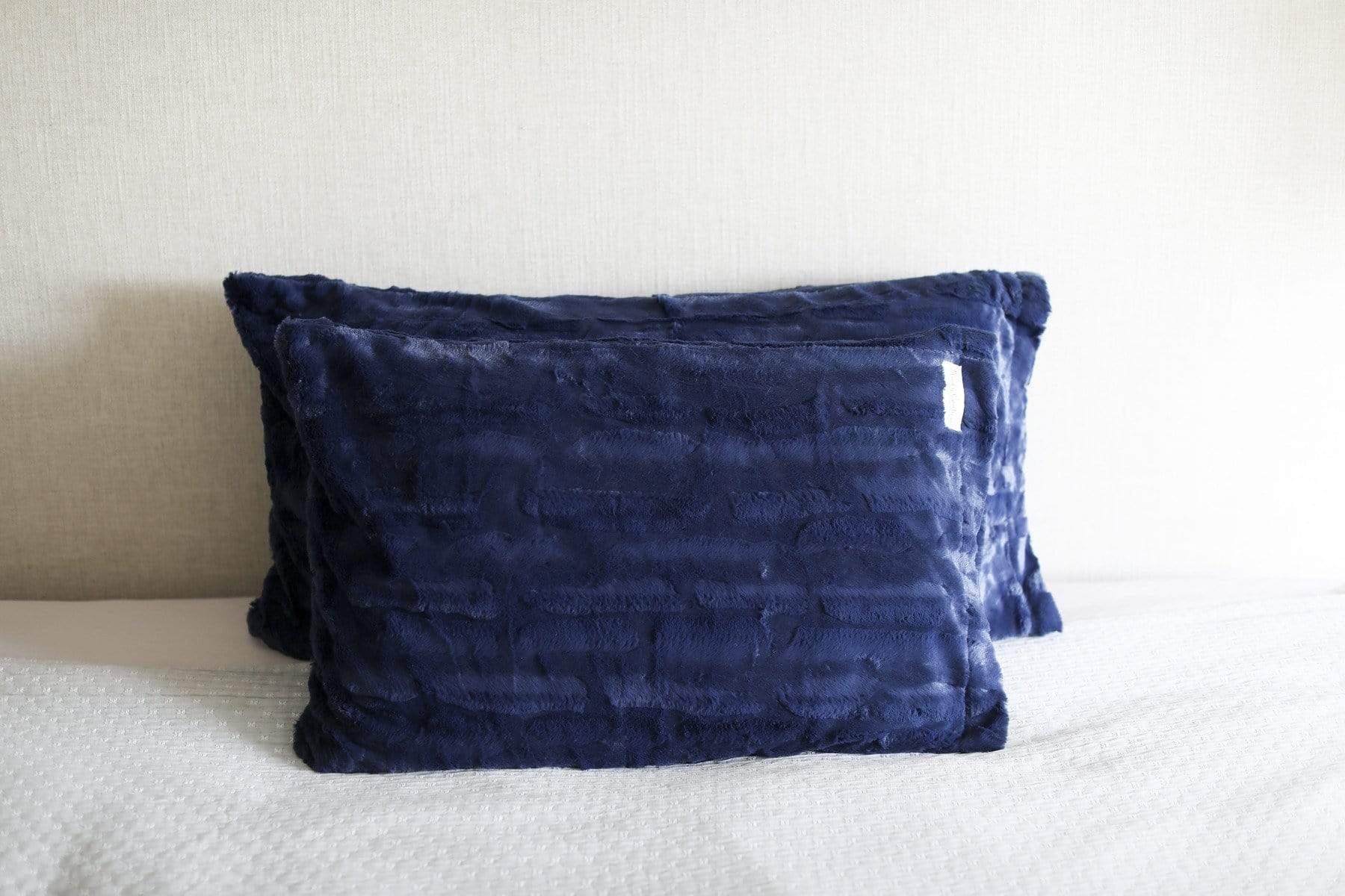 Two plush navy pillows by Minky Couture on a bed. 