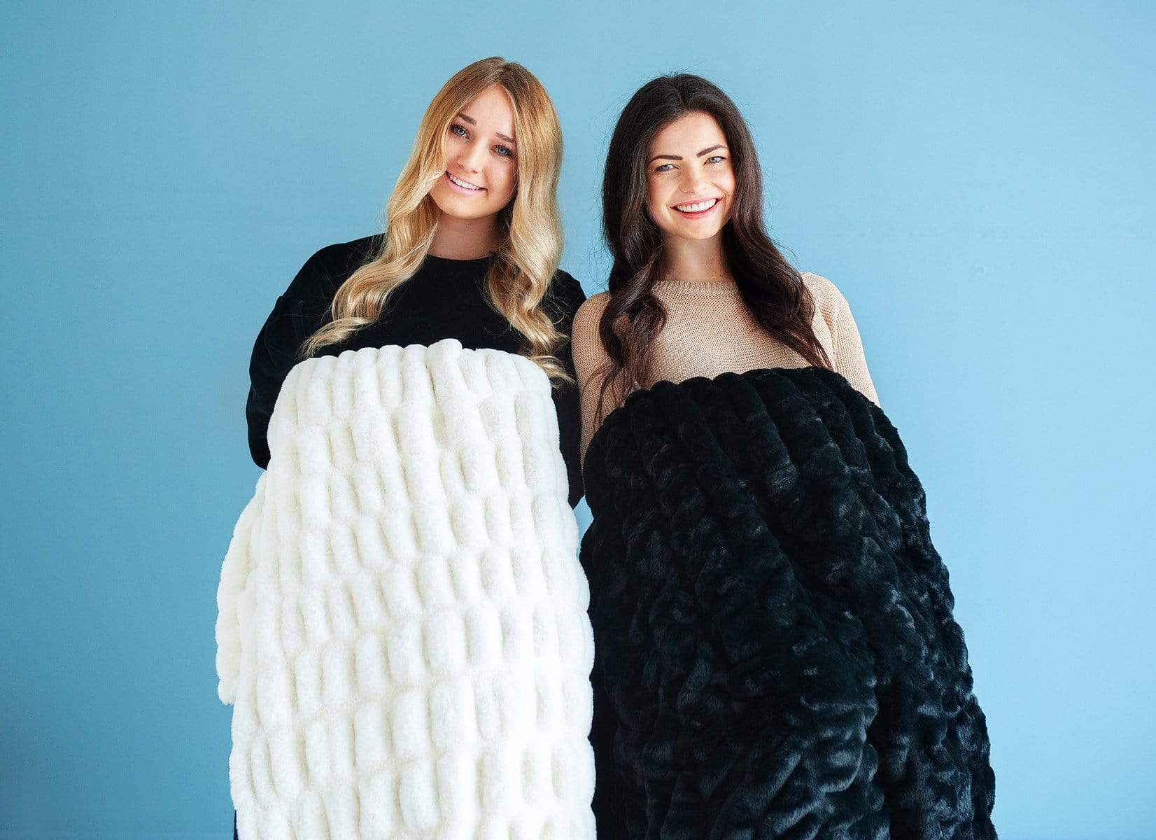 Two women holding a black and cream stretchy hugs blanket by Minky Couture. 