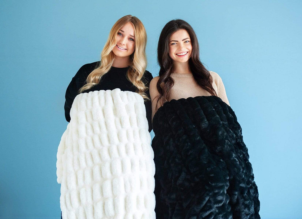 Two women holding a black and cream stretchy hugs blanket by Minky Couture. 