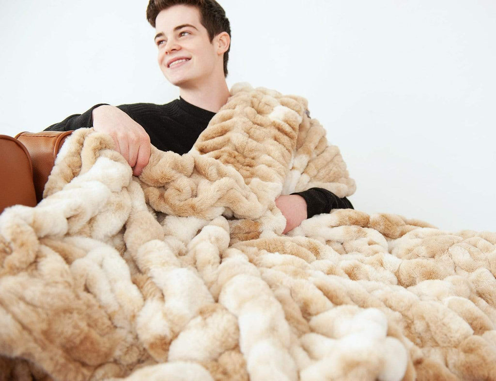 Young man sitting on a couch covered up with his Cotton Candy Caramel stretchy hugs blanket by Minky Couture. 