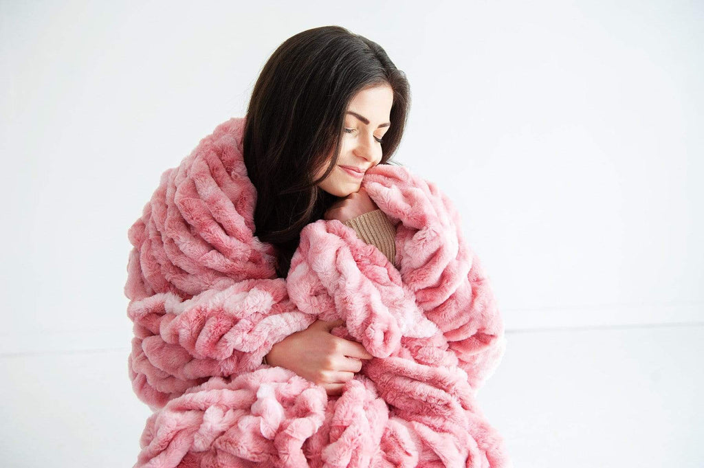 Young woman sitting wrapped up in the stretchy and cozy pink hugs blanket by Minky Couture. 