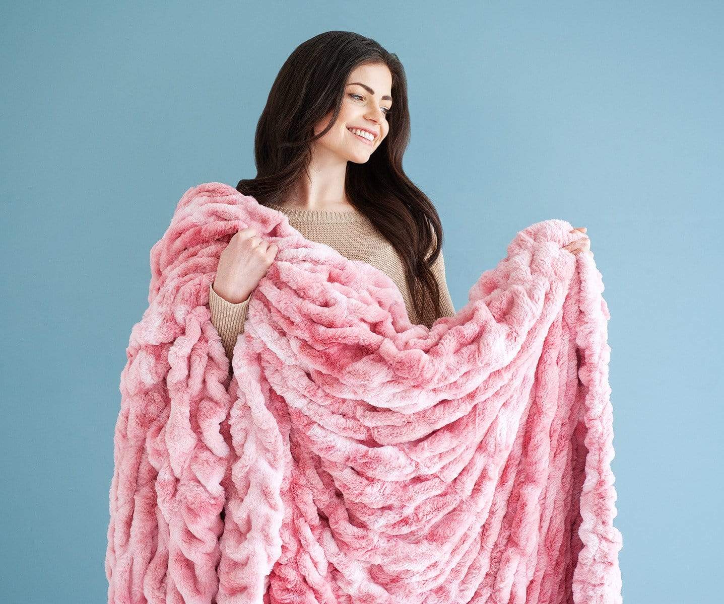 Woman standing against a blue wall holding a pink stretchy hugs blanket by Minky Couture.