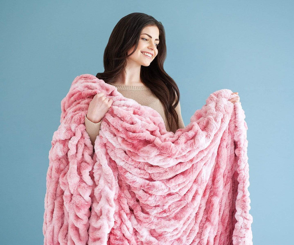 Woman standing against a blue wall holding a pink stretchy hugs blanket by Minky Couture.