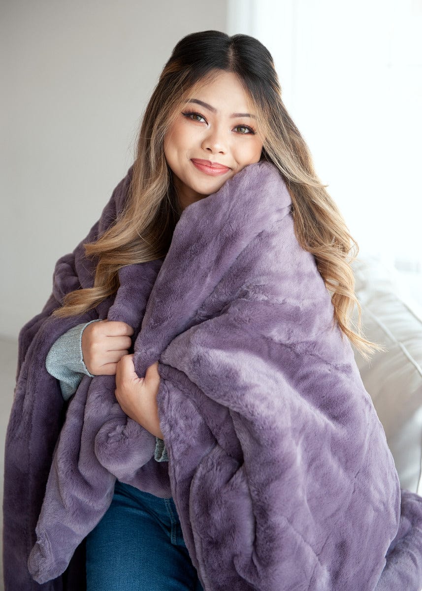 Young woman wrapped up in a heather purple thick plush blanket.