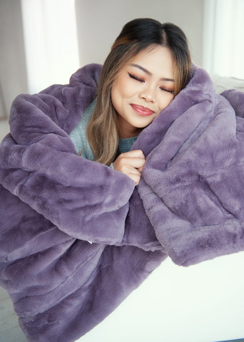 Young woman wrapped up in a heather purple thick plush blanket.