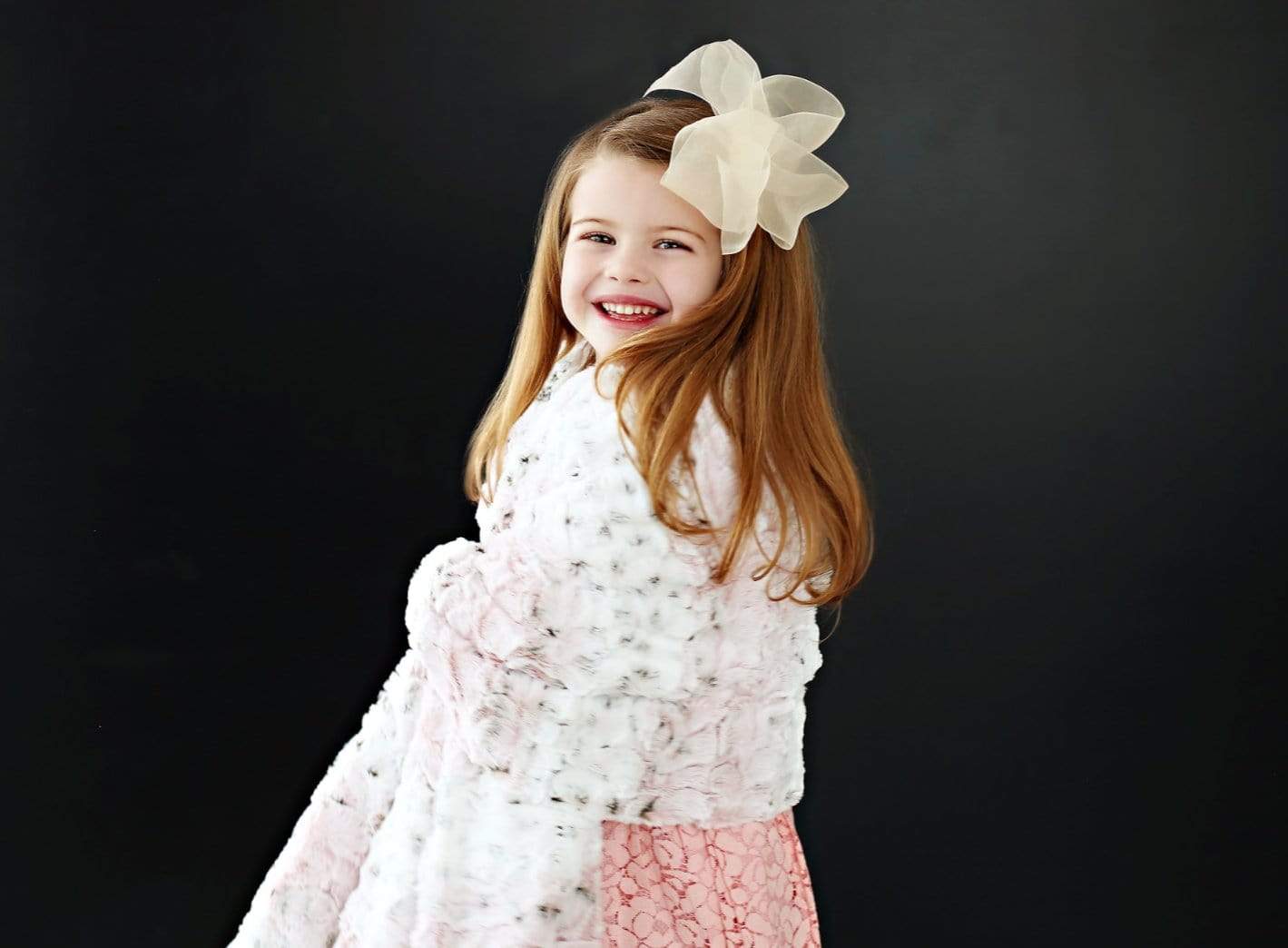 Girl with a large pink bow on her head snuggled up in a pink sandra blanket by minky couture.