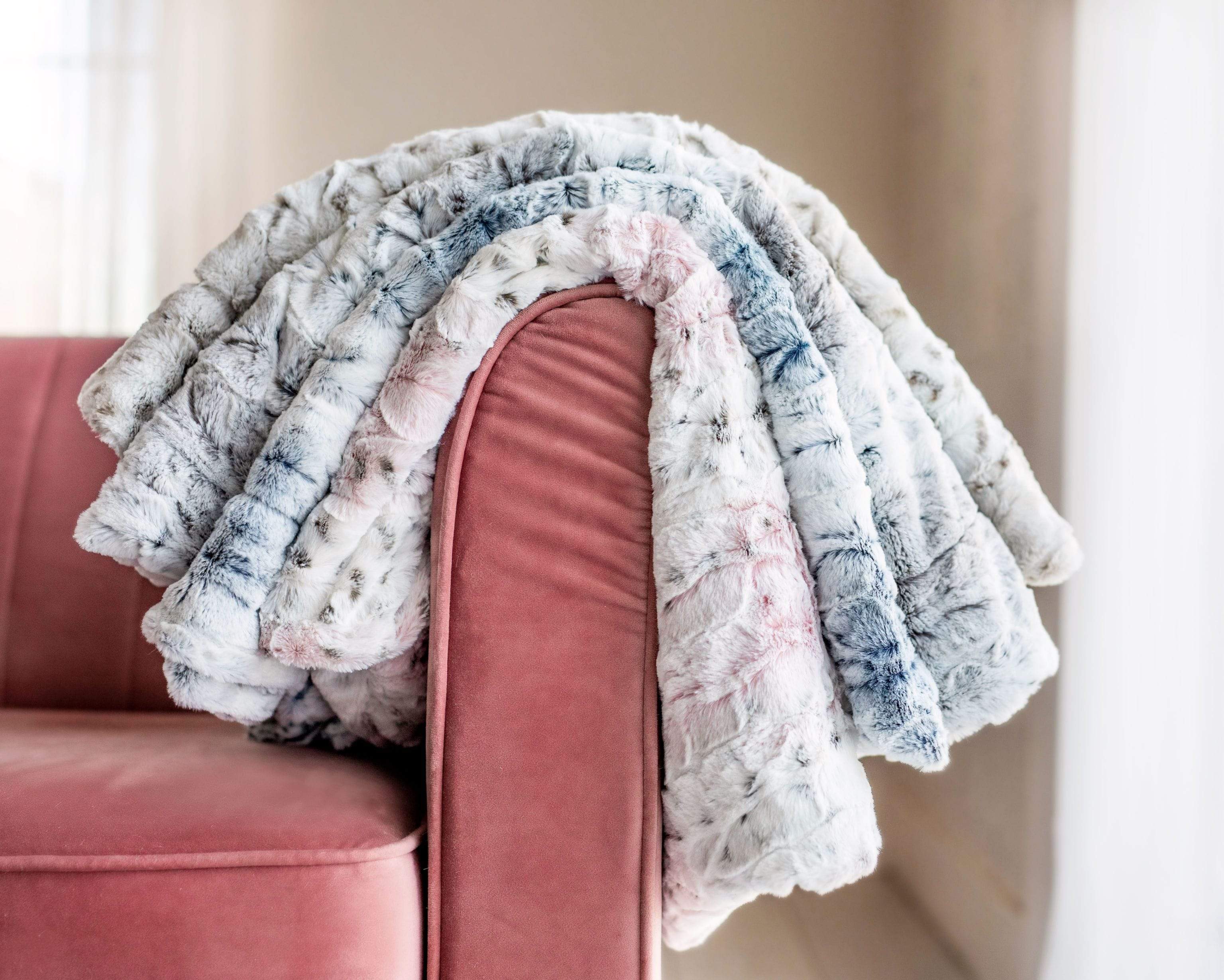 Four colorways of the Sandra blanket by Minky Couture laid over the arm of a mauve couch.