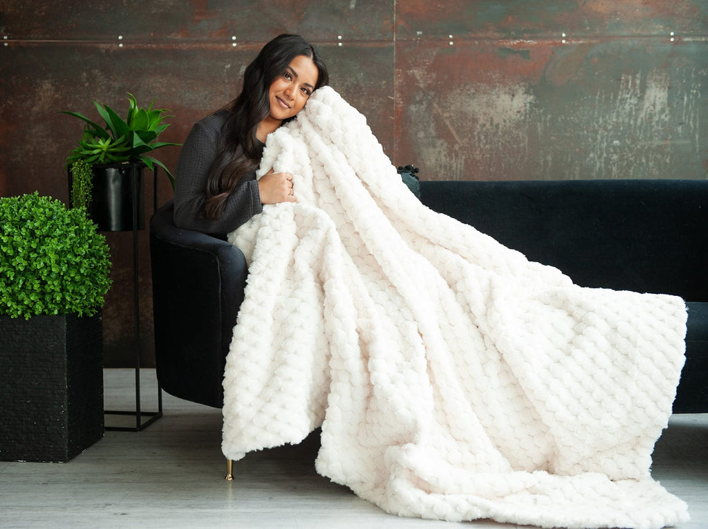 Young woman on a black couch holding a cream waffle textured blanket.