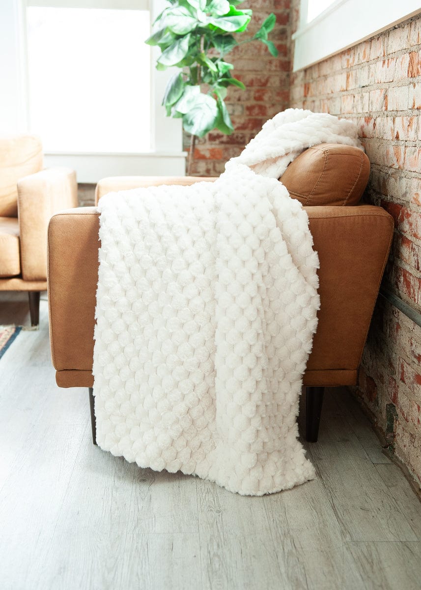 Cream waffle textured blanket hanging over the side of a brown leather couch.