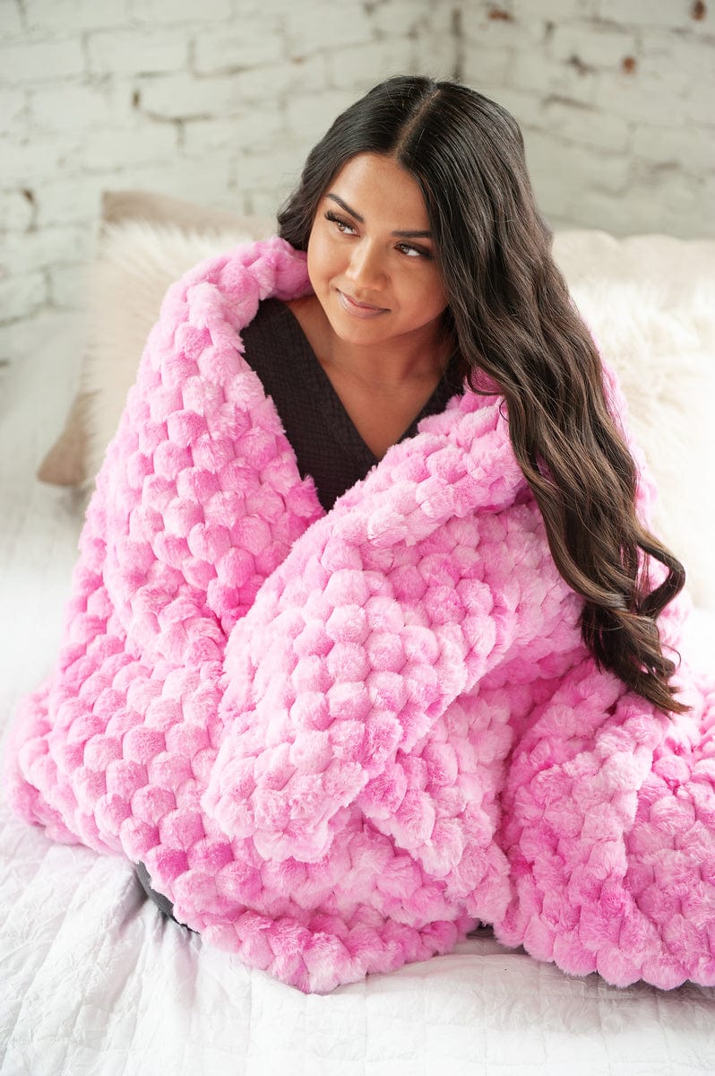 Young women sitting on a bed holding a pink waffle textured blanket.