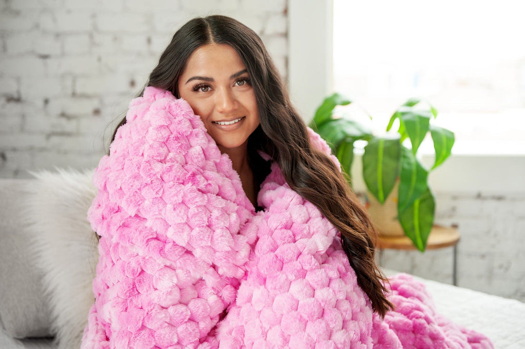 Young women holding a pink waffle textured blanket.
