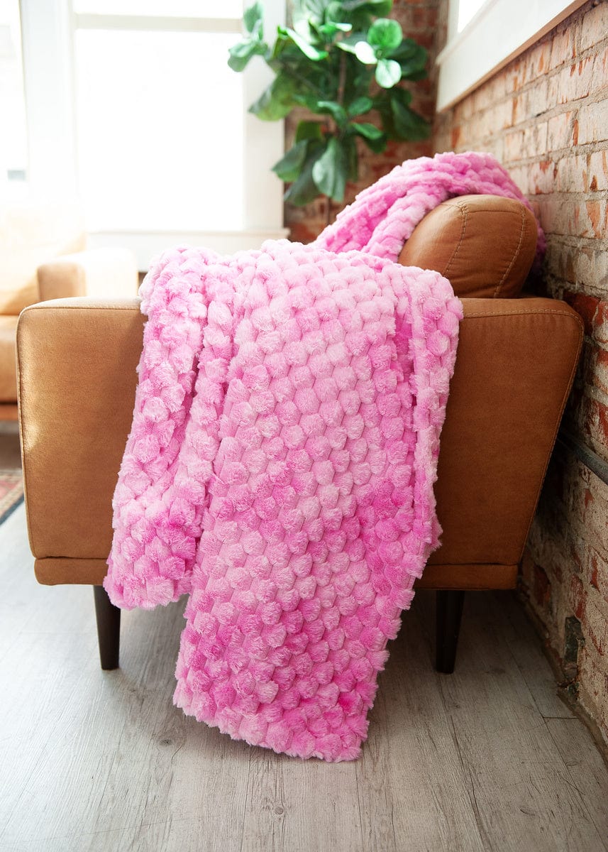 Pink waffle textured blanket draped over the side of a brown leather couch,