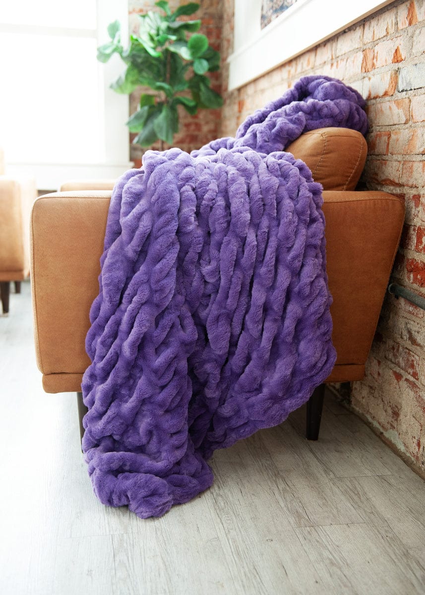 Vibrant purple ruched blanket laid on a brown leather couch.