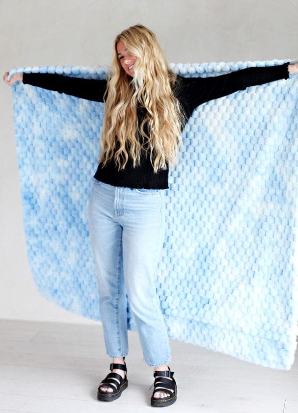 Young woman holding a light blue waffle textured blanket behind her back. 
