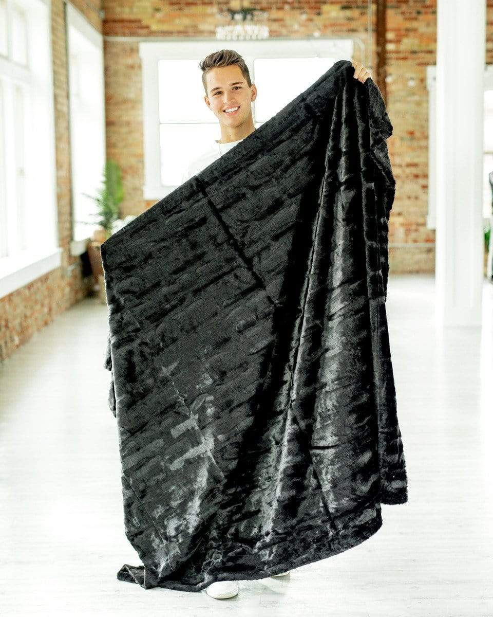 Young man holding a silky black plush blanket by Minky Couture. 