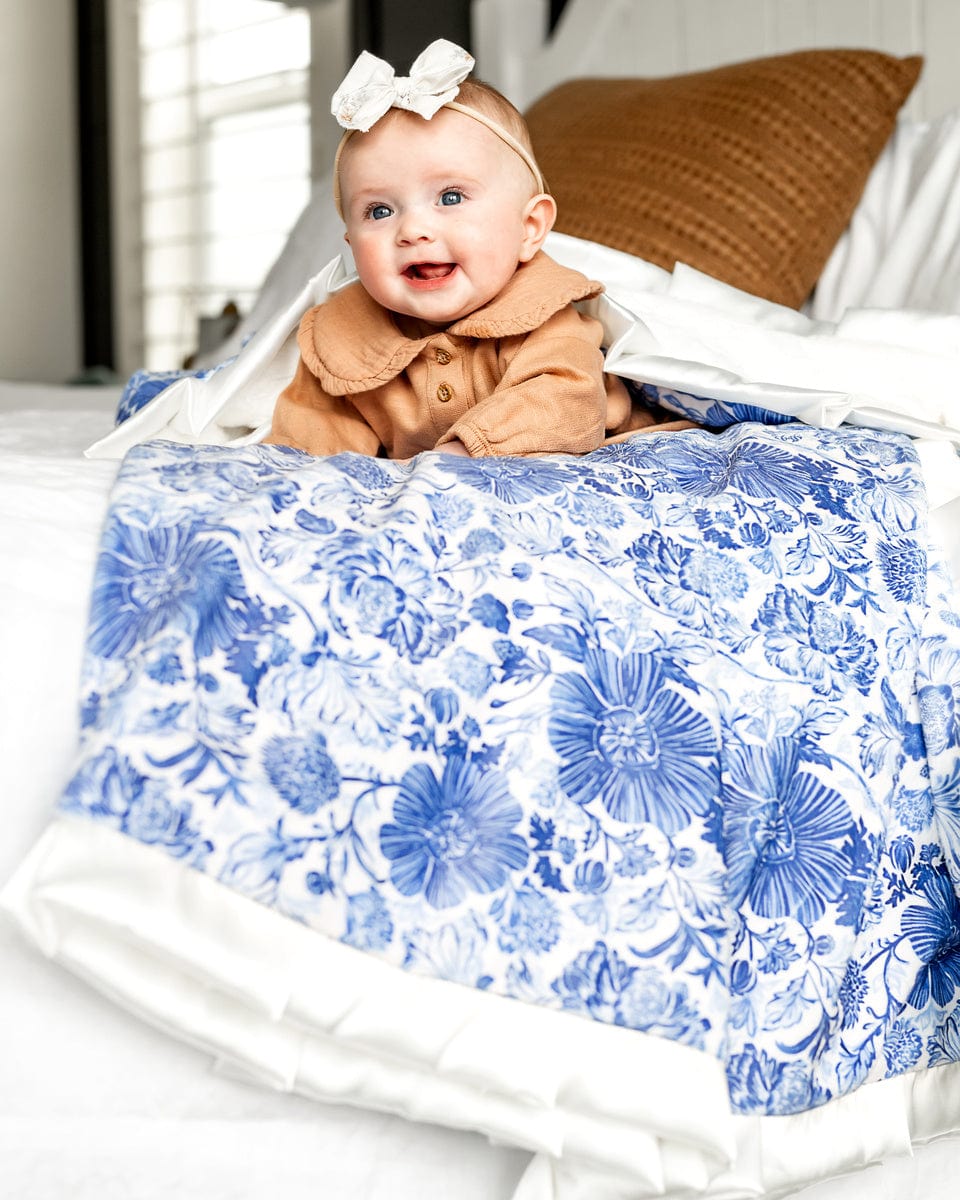Baby girl laying on a blue floral patterned blanket on top of a bed.