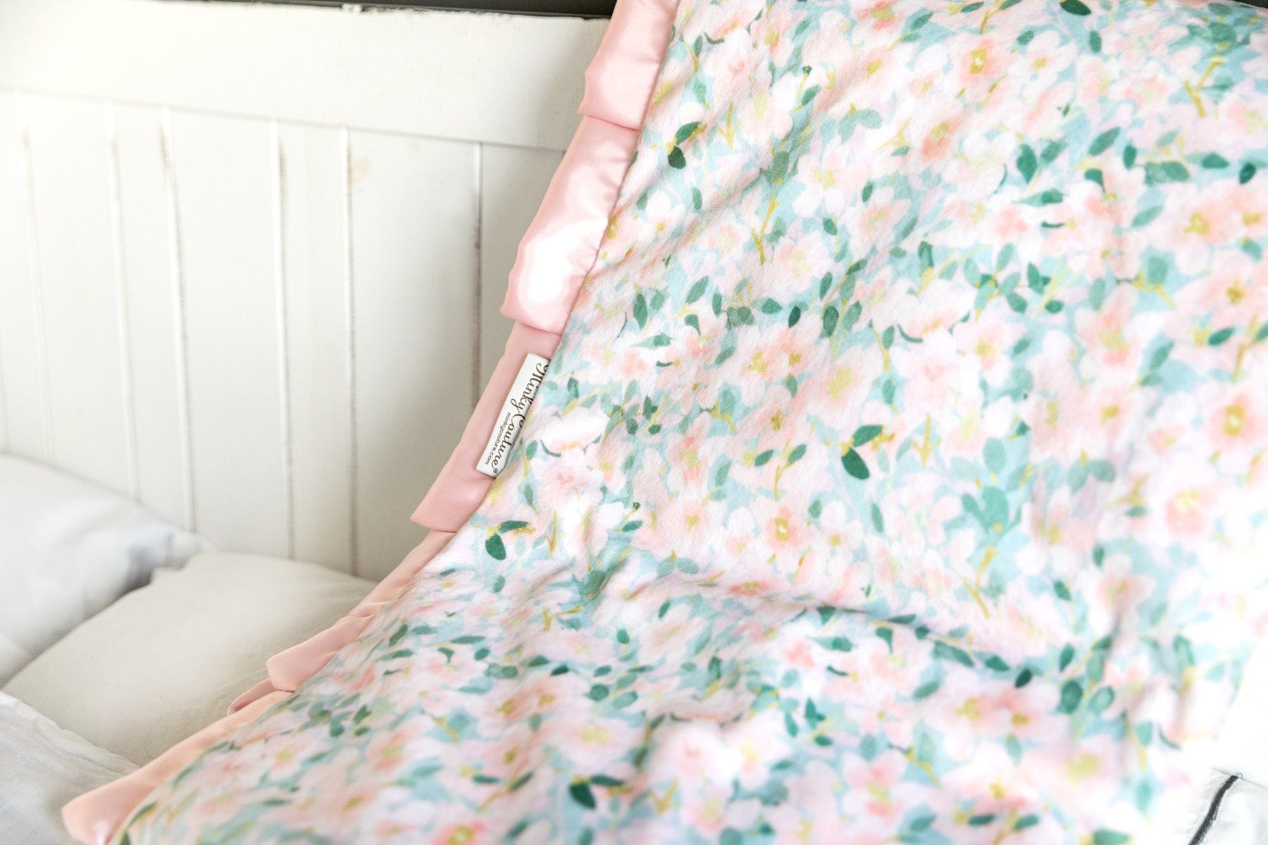 Minky Couture blanket with pink flowers on a blue background laid over a couch.