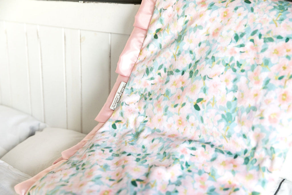 Minky Couture blanket with pink flowers on a blue background laid over a couch.