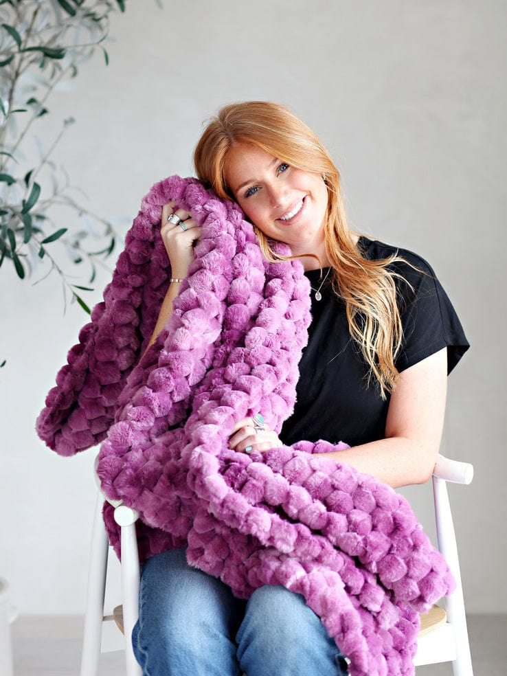 Young woman sitting while holding a purple waffle textured blanket by Minky Couture. 