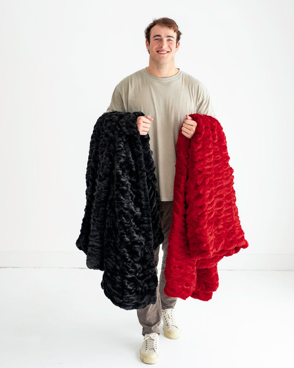 Man standing with a red blanket over one arm and a black blanket over the other.