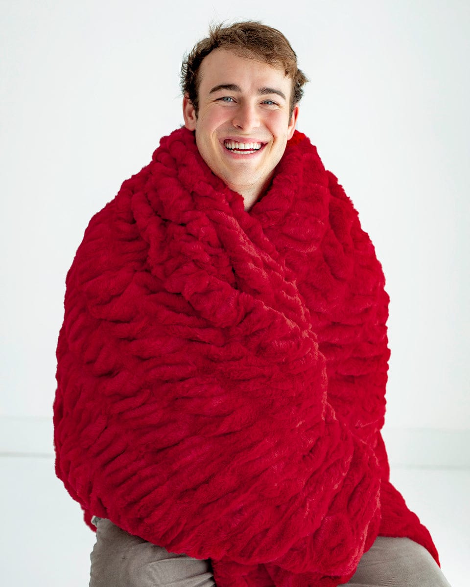 Man sitting while wrapped up in a red ruched plush blanket. 