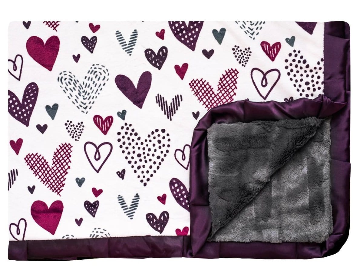 Love Notes - Plum Minky Couture designer blanket laying flat with edge turned up. Doodled purple hearts with charcoal faux fur back and plum satin ruffle. 