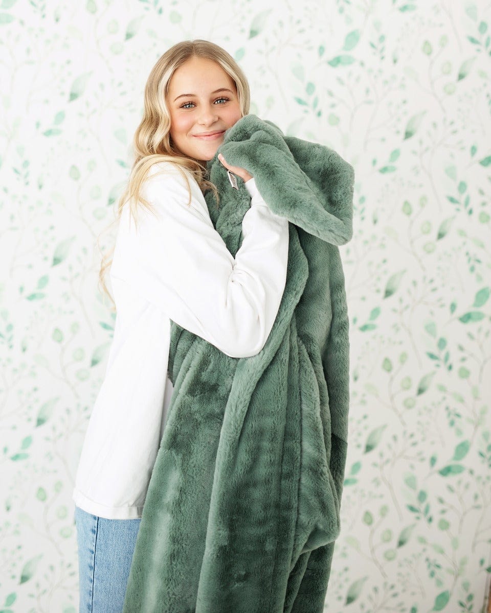 Young woman holding a mist green plush blanket near her face.