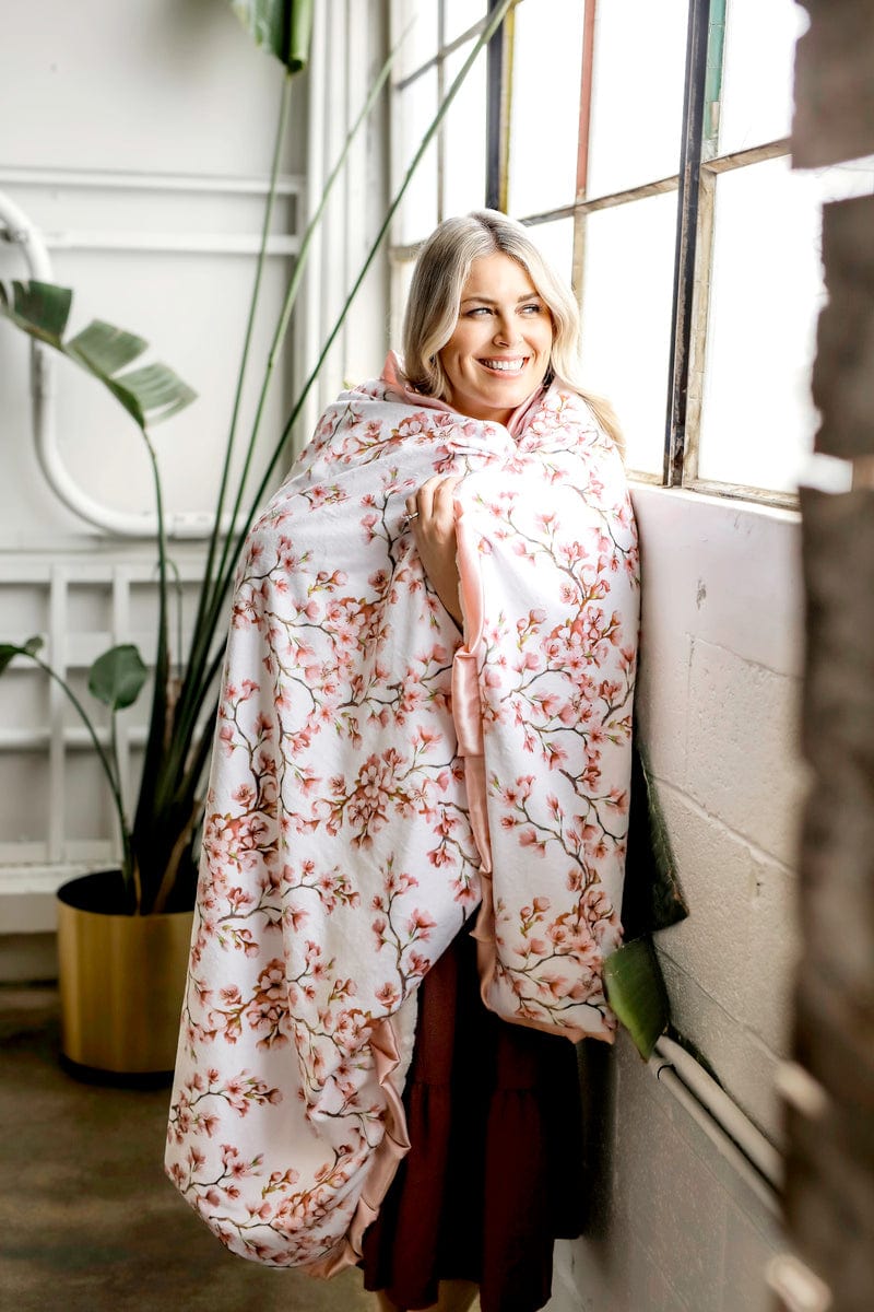 Woman standing next to a window wrapped in a cherry blossom themed Minky Couture blanket. 