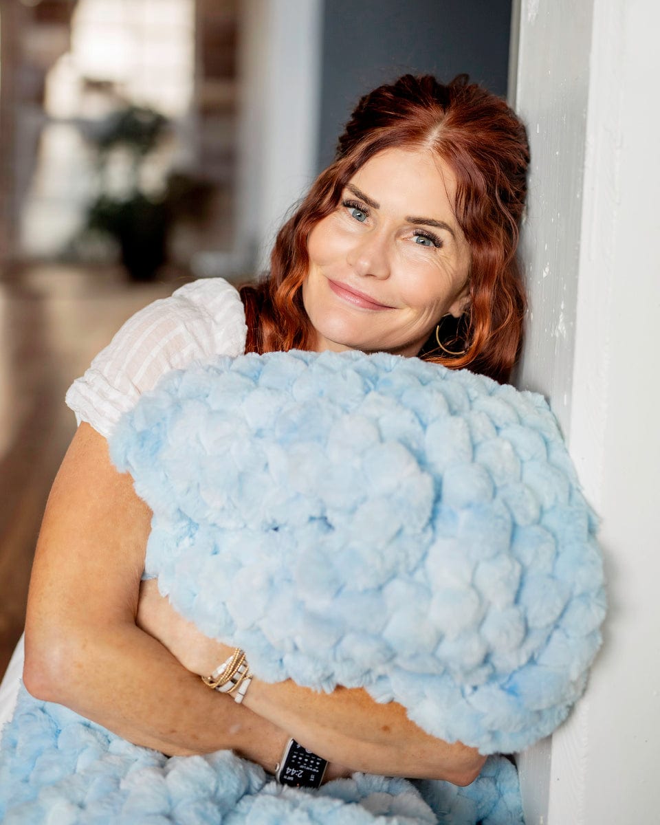 Woman leaning against a wall holding a light blue waffle patterned blanket. 