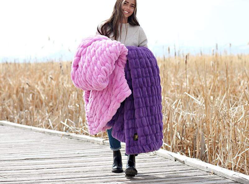 Young woman walking along a wooden boardwalk holding bright pink and purple stretchy hugs blanket by Minky Couture. 