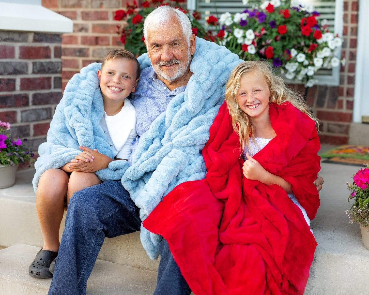 Grandfather sitting on porch steps with two grandchildren holding blue and red Minky Couture blankets. 