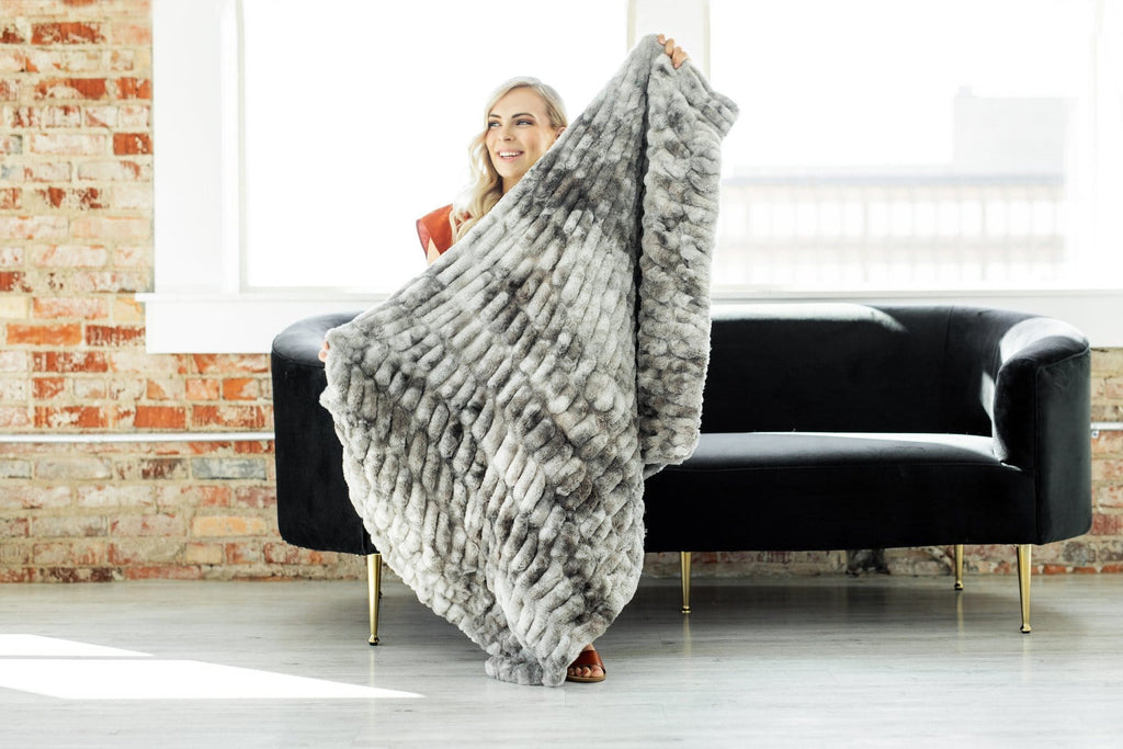 Woman sitting on a black couch holding a tie dye gray and charcoal blanket in front of her. 