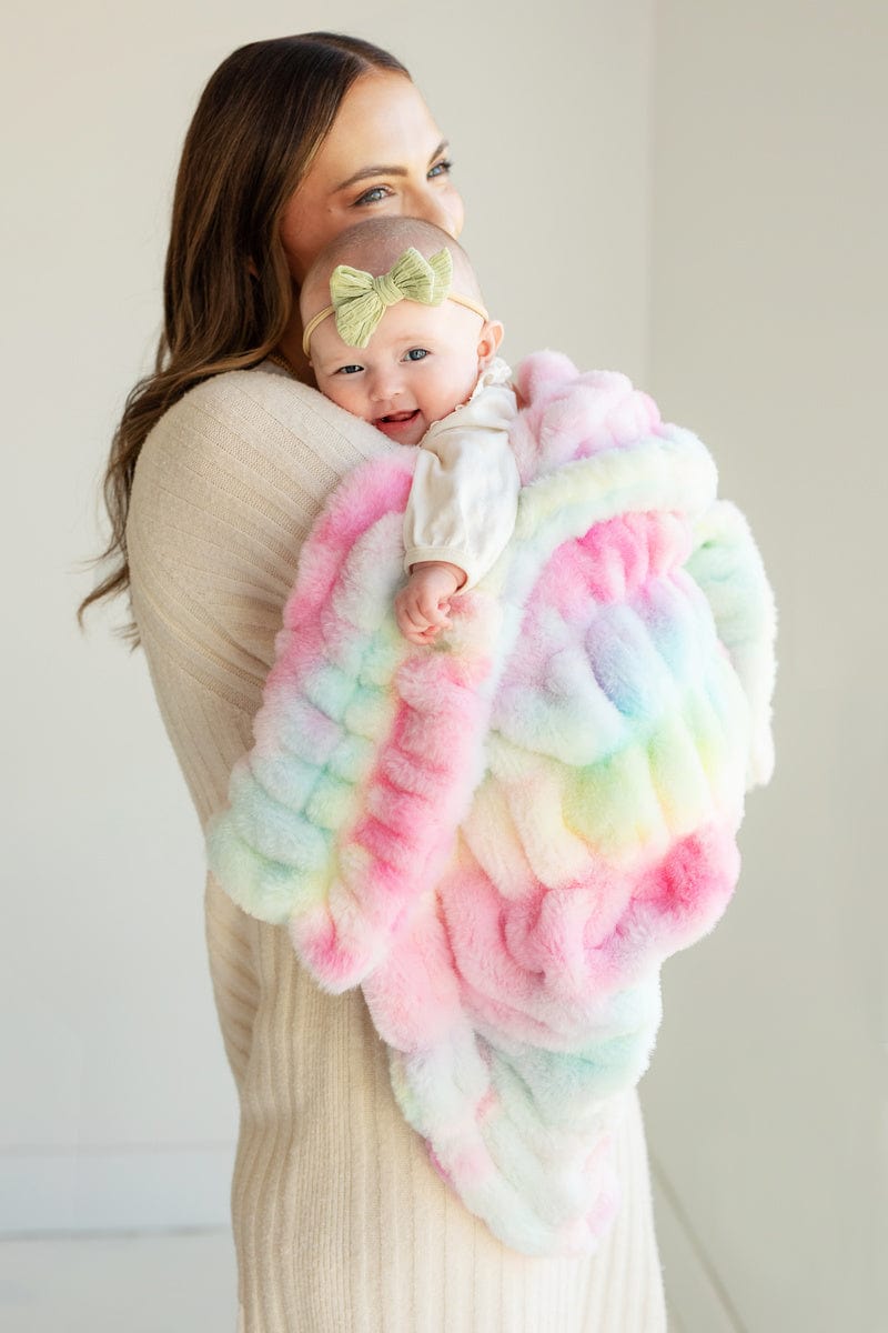 Young mom holding her baby wrapped up in a tie dye pastel stretchy blanket.